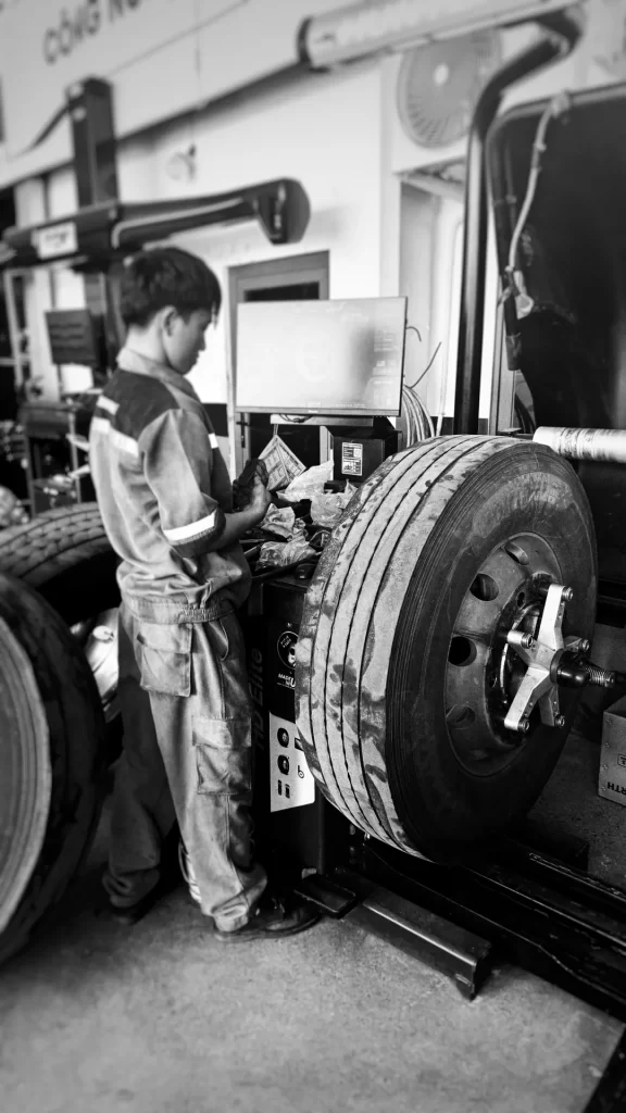 A technician performing a dynamic wheel balancing procedure on a commercial truck steer tire using a Hunter HD Elite balancer machine in a workshop.