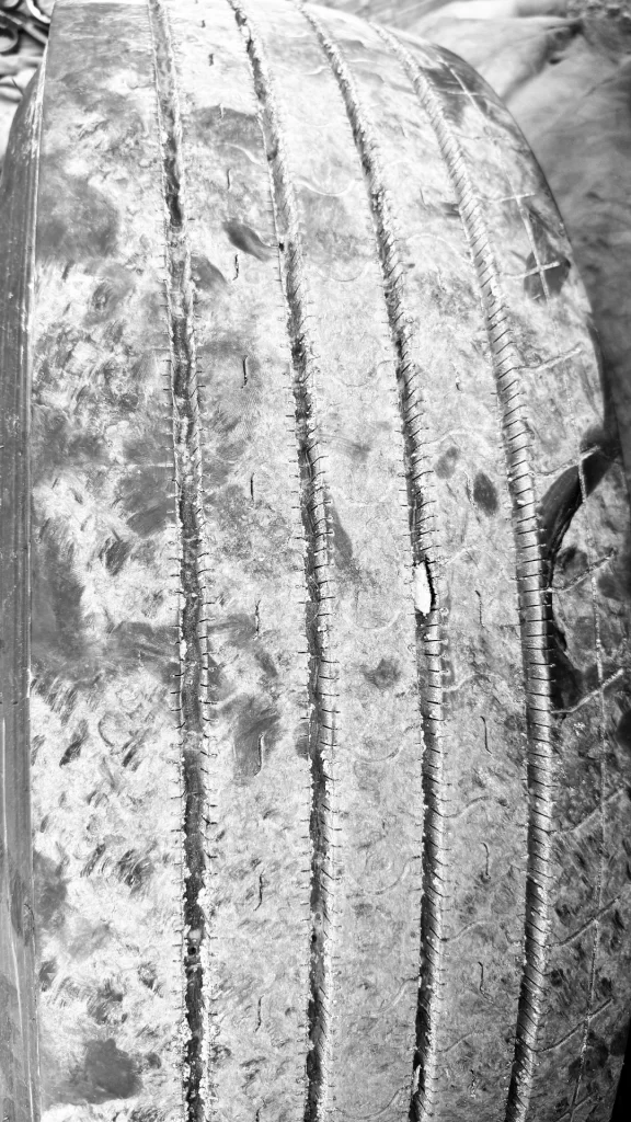 A commercial truck steer tire showing severe one-sided shoulder wear on the left side while the right shoulder still retains visible tread patterns and sipes.
