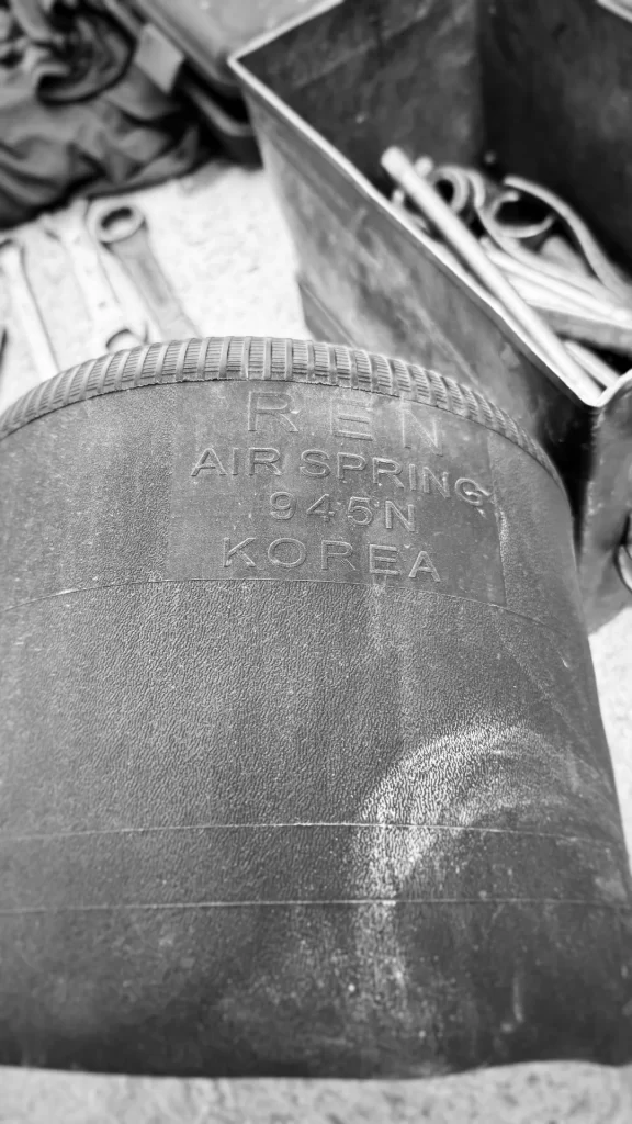A worn commercial truck suspension air spring from R.E.N Korea showing signs of rubber aging and cracking, scheduled for replacement during maintenance.